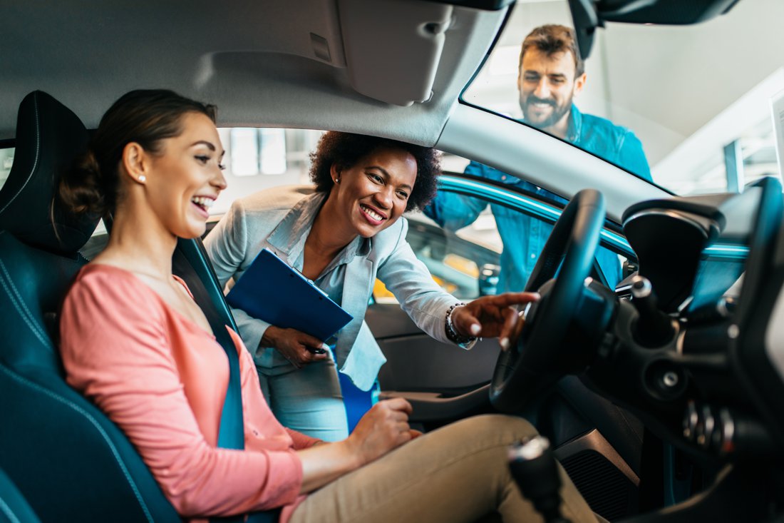 Woman sitting in car in dealership shwroom. A woman and a man are showing her the car.